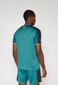 Türkiz sportpóló fekete díszítéssel, rövid ujjú, zöld szegéllyel. Könnyű anyag, sima tapintású. Logó a hátközép részen, a nyakkivágásnál.