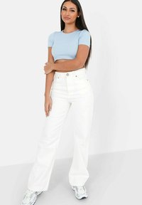 Lys blå ribbet crop top, højtaljede hvide vide jeans og grå sneakers. Glat tekstur med klassisk knaplukning og lommer.
