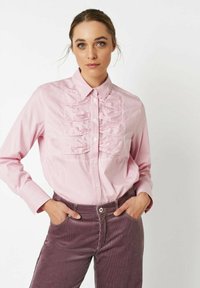 Pink striped button-up shirt with ruffled front detail, long sleeves, and a classic collar, paired with dark purple corduroy pants.