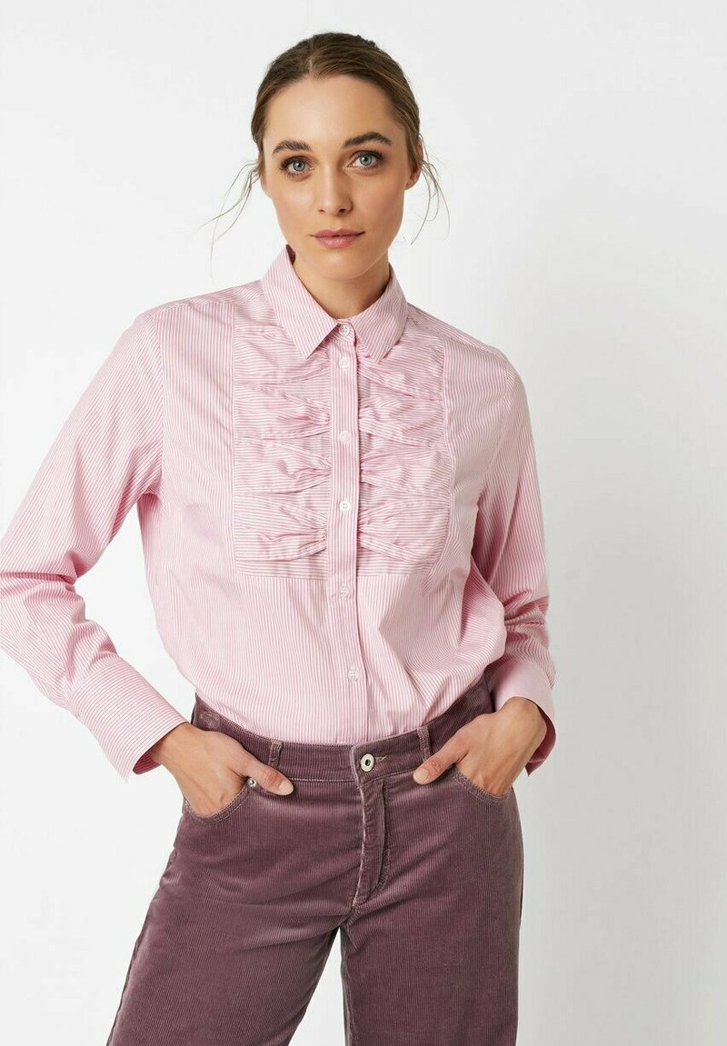 Pink striped button-up shirt with ruffled front detail, long sleeves, and a classic collar, paired with dark purple corduroy pants.