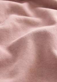 Tessuto di cotone rosa chiaro con una consistenza morbida, caratterizzato da sottili variazioni di tonalità e pieghe delicate, che creano un aspetto drappeggiato.