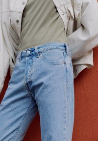 Ljusblå denimjeans med rak passform, femfickdesign och subtila blekningar vid låren. Matchas med en grå topp och en vit jacka.