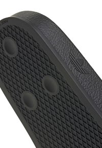 Semelle de chaussure en caoutchouc noir avec motif de grip texturé, deux protubérances rondes et un logo Adidas trefoil embossé sur le bord latéral.