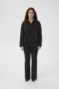 Svart langermet genser med krage, med en subtil, teksturert mønster, paret med svarte utslåtte jeans og spisse sko.