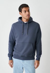 Tamsiai mėlynas džemperis su gobtuvu, priekyje kišenė, reguliuojamos raišteliai, pasiūtas iš minkštos medvilnės mišinio medžiagos, turi ribotas rankogalių detales. Laisvo stiliaus, kasdieniškas dizainas.