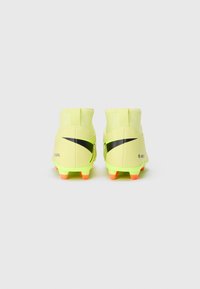 Botas de fútbol amarillas con una superficie texturizada, franjas de acento negras y tacos naranjas. Presenta un diseño de tobillo alto y un talón reforzado.