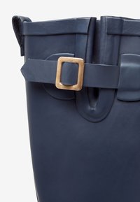 Marineblauwe rubberen bucket bag met een matte afwerking, voorzien van een goudkleurige rechthoekige gesp en twee afgeronde zijopeningen.