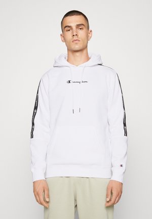 Sudadera blanca con un bolsillo canguro en la parte frontal, capucha con cordones y logo negro. Presenta rayas de marca negra a lo largo de las mangas. Material de algodón.