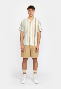 Short-sleeve, collared shirt in pastel stripes of blue, yellow, and gray; paired with beige shorts, white sneakers, and striped socks.