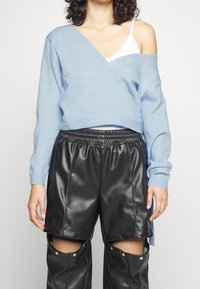 Jasnoniebieski, oversize sweter z dekoltem w serek, wykonany z miękkiego materiału; zestawiony z czarnymi skórzanymi szortami z zatrzaskami i elastycznym paskiem.