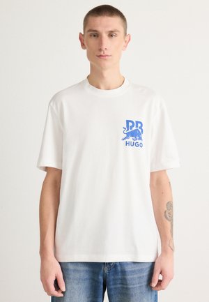 T-shirt bianca in cotone con collo rotondo, maniche corte e una stampa grafica blu raffigurante un toro e loghi sul lato sinistro del petto.