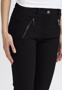 Crne krojene hlače s glatkom teksturom, s patentnim zatvaračem na džepovima i prilagođenim dizajnom s minimalnim šavnim detaljima, prikazane na visini struka.