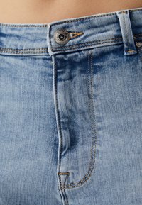 Svijetloplavi traperice, visoki struk s kontrastnim šavovima, s metalnim gumbom i zatvaračem, te teksturiranom završnom obradom.