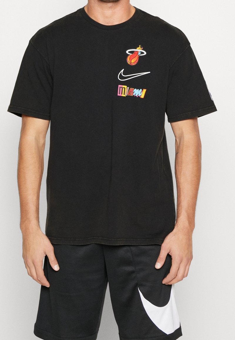 Camiseta de algodón negra con el logo de Miami Heat, texto vibrante "Miami" en varios colores y el swoosh de Nike. Diseño de mangas cortas y cuello redondo.