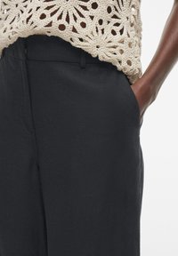 Top de ganchillo beige superpuesto sobre pantalones anchos de navy oscuro con bolsillos laterales, que presenta una textura suave y un diseño ajustado.
