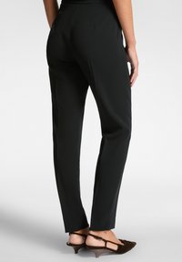 Pantalones negros ajustados de corte entallado, con una textura suave y una cinturilla de altura media, combinados con sandalias marrones de tacón.