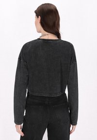 Maglietta nera a maniche lunghe con una trama sbiadita, dotata di scollo rotondo e dettagli di cucitura, abbinata a jeans neri a vita alta.