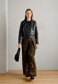 Veste de biker en cuir noir avec des zip argentés, associée à un pantalon large en imprimé léopard aux tons terreux et un sac à main noir.