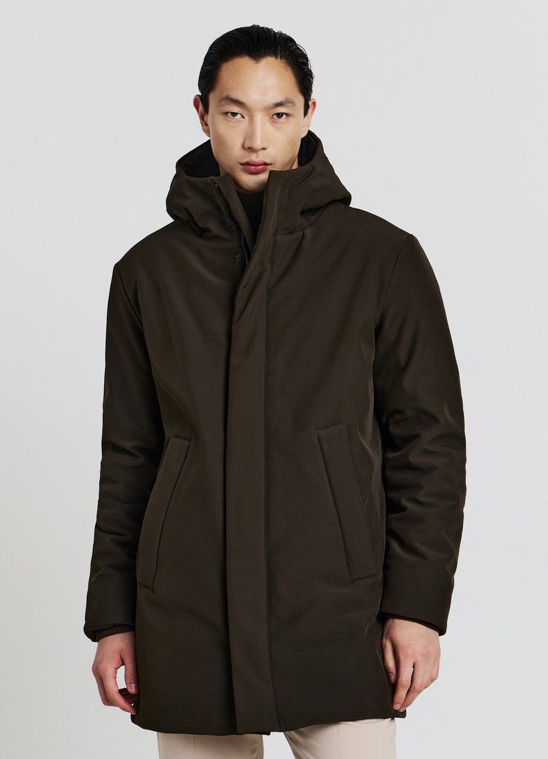 Cappotto verde scuro con cappuccio e silhouette dritta, dotato di due tasche laterali e una texture morbida. Davanti chiuso con dettagli hardware minimi.