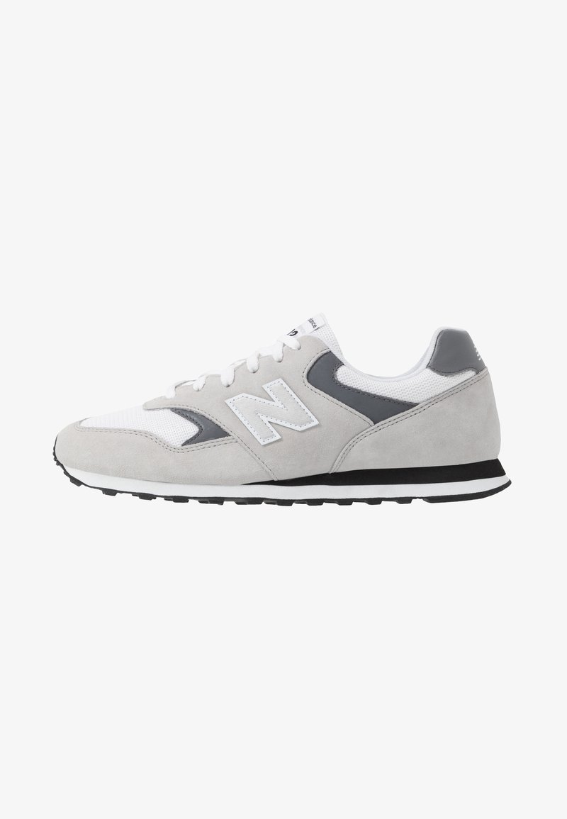 Baskets New Balance grises et blanches avec des matériaux en suède et en mesh, semelle noire et blanche, et logo sur le côté.