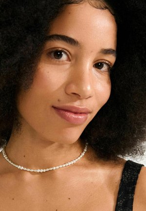 Pearl necklace featuring round, lustrous pearls with alternating larger and smaller sizes, paired with a dark lace top.