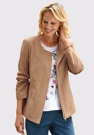 Veste en faux suède beige avec un col rond, deux poches latérales zippées et des manches trois-quarts, associée à un haut à imprimé floral et à un jean bleu.