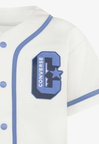 Camisa blanca de manga corta con acentos azules, que presenta un logo de goma azul con la inscripción "CONVERSE" y una gran "C" con una estrella.