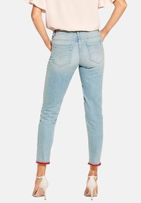 Helle blaue Denim-Jeans mit taillierter Passform, Fünf-Taschen-Stil und roten Fransenakzenten am Saum. Tragen Sie dazu weiße High Heels.