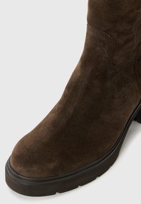 Bruine suede enkellaars met een ronde neus, platte rubberen zool en subtiele stiksels langs de zijkanten. Gladde, gestructureerde oppervlakte.