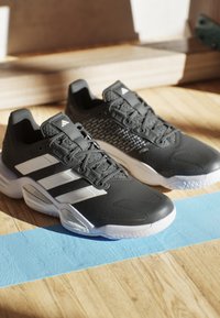 Black athletic shoes with three white stripes, textured upper, and cushioned sole. Features lacing system and rubber outsole, designed for stability.