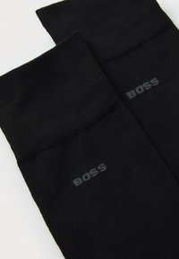 Schwarze Socken aus strukturiertem Stoff, mit einem gerippten Bündchen und einem kleinen, grauen "BOSS"-Logo auf jeder Socke.