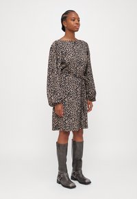 Haljina s leopard uzorkom u bež i crnoj boji, s dugim rukavima i vezanjem u struku. Uparena sivoj čizmama do koljena s kopčama.