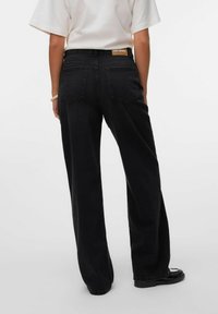 Zwarte wijde jeans met een hoge taille en twee achterzakken. Voorzien van een bruine leren merklabel aan de tailleband. Soepele dennenstof.