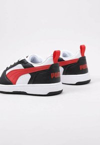 Sneaker nere e rosse con suola bianca, pelle texturizzata e un prominente logo PUMA sul tallone e sul lato. Accenti rossi sulla linguetta.