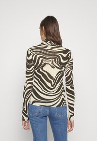 Langärmliges Oberteil mit einer taillierten Silhouette, das ein abstraktes, wellenförmiges Muster in Schwarz und Creme aufweist, gefertigt aus einem weichen, dehnbaren Stoff.