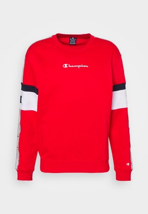 Červená mikina má kulatý výstřih, dlouhé rukávy a bílé a námořnické akcenty. Na hrudi je bílé logo "Champion". Měkká textura.
