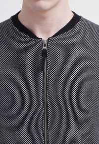 Svart och vitt mönstrad zip-up tröja med ribbad krage och textil med en subtil geometrisk design.