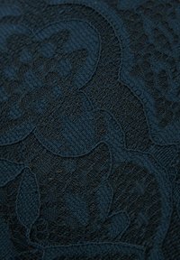 Mörkblått tyg med ett präglat blommönster, som har varierande texturer och intrikata detaljer. Slät och subtilt reflekterande yta.