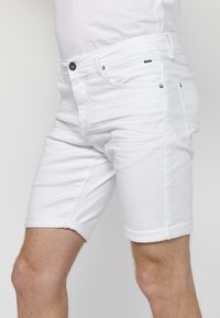 Pantalones cortos de mezclilla blanca con dobladillos enrollados, que cuentan con cremallera, cierre de botón y dos bolsillo delanteros. Textura suave con ligera elasticidad.
