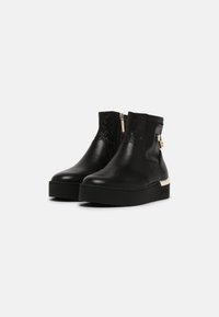Botas de tobillo de cuero negro con detalles en relieve, herrajes en tono dorado, cremallera lateral y suela gruesa negra.
