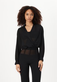 Blusa leggera nera con design a fascetta, maniche lunghe e scollatura a V, abbinata a pantaloni neri a vita alta con dettagli trasparenti.