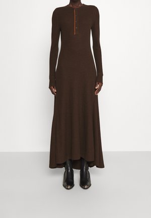 Brązowa sukienka z długim rękawem wykonana z miękkiego materiału, z okrągłym dekoltem z zapięciem na guziki i rozkloszowanym dołem. Dobierz do niej czarne botki za kostkę.