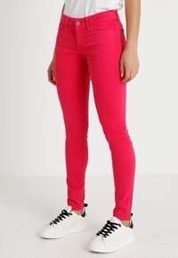 Skinny Jeans aus dehnbarem, pinkem Stoff, mit figurbetontem Design, Fünf-Taschen-Stil und einem einzelnen Knopf- und Reißverschluss.