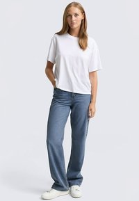 Bijela pametna majica kratkih rukava, opuštenog kroja, u kombinaciji s trapericama ravnog kroja u srednje plavoj boji i bijelim tenisicama. Jednostavan, ležeran dizajn.