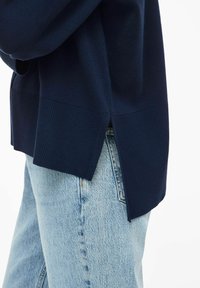 Pull en maille bleu marine avec une texture côtelée, des fentes latérales et une coupe décontractée, associé à un jean en denim bleu clair.