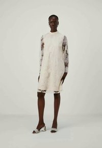 Φόρεμα από δαντέλα με μακριές δαντελένιες μανσέτες, μήκους μέχρι το γόνατο, σε εκρού απόχρωση. Μαλακό ύφασμα με λουλουδένια σχέδια. Συνδυασμένο με ασημένιες ψηλοτάκουνες σανδάλια.