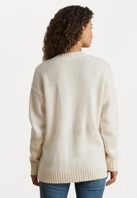 Sweater oversized em creme com bainha e decote canelados, apresentando um padrão de malha texturizado. As costas mostram um ajuste solto e descontraído.