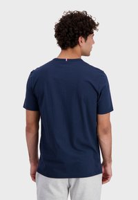 Navy blue short-sleeve t-shirt made of cotton, featuring a round neckline and a small colored accent at the back.