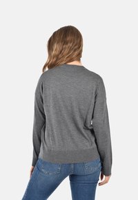 Maglione grigio realizzato in morbido tessuto, con girocollo e bordo a coste, abbinato a jeans blu scuro. La vista posteriore mostra una vestibilità rilassata.