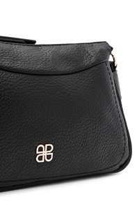 Borsa a mano in pelle nera con superficie texture, parte superiore curvata e accento logo in tonalità oro sul davanti. Presenta un design a patta pieghevole.
